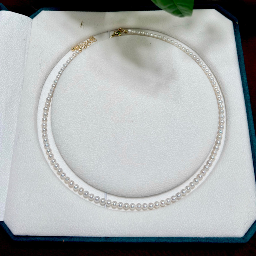 A shinny pearl necklace with gold-toned chain details and clasp, displayed inside an open white jewelry box.
