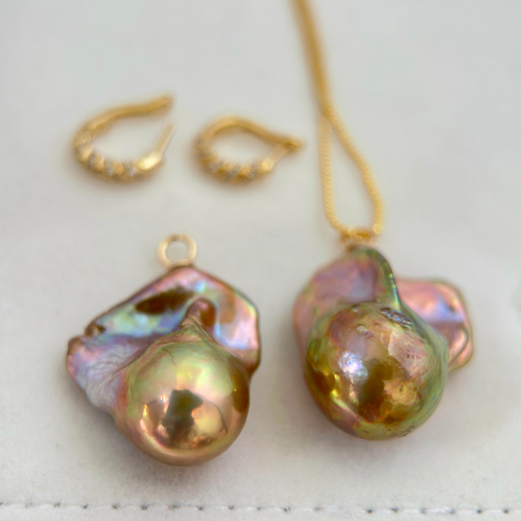 A gold jewelry set featuring a necklace and matching earrings with large, baroque-style iridescent pearls on a soft white background.