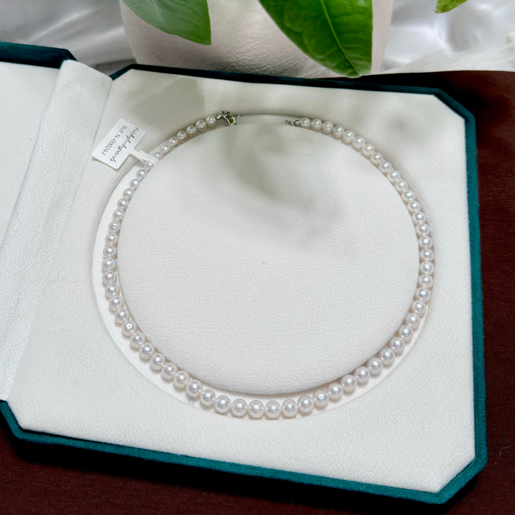 A double-row pearl necklace displayed inside an open dark teal jewelry box with a white velvet interior. The necklace consists of small, round, lustrous white pearls strung closely together, with a small silver clasp visible at the top.