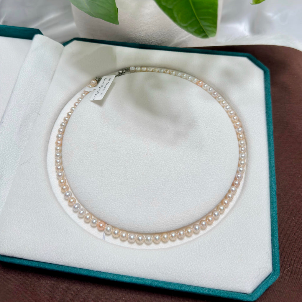 A double-strand pearl necklace with warm cream and light peach pearls, displayed inside an open teal jewelry box with a white velvet interior.