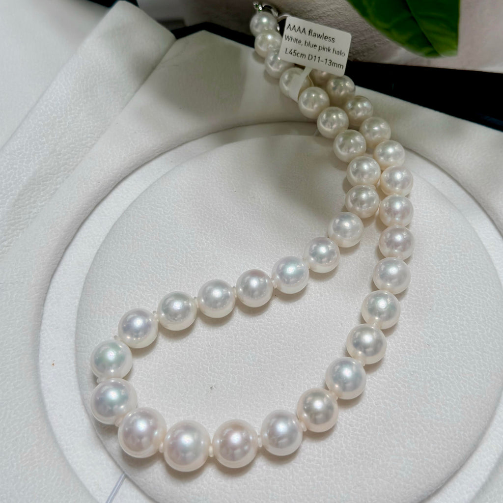 A single-strand pearl necklace with large, round, lustrous white pearls, displayed on a white circular jewelry stand.