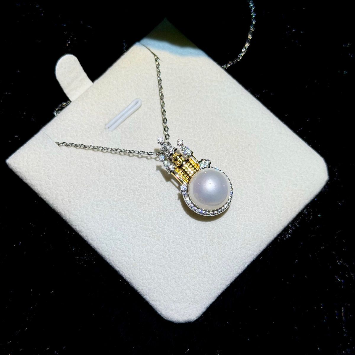Close-up of a white freshwater pearl beneath a detailed castle pendant.