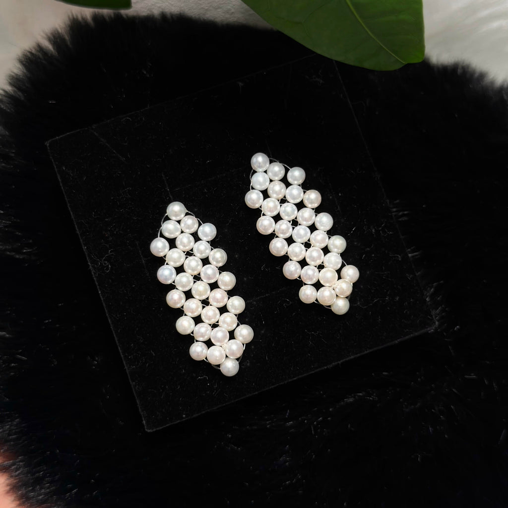 
White freshwater pearl dangle earrings arranged in a delicate woven pattern.
