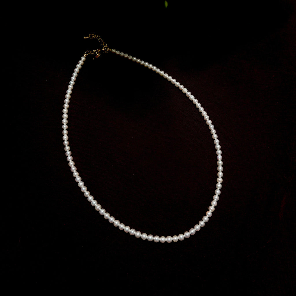 A single-strand pearl necklace with a gold clasp, displayed on a dark black background.