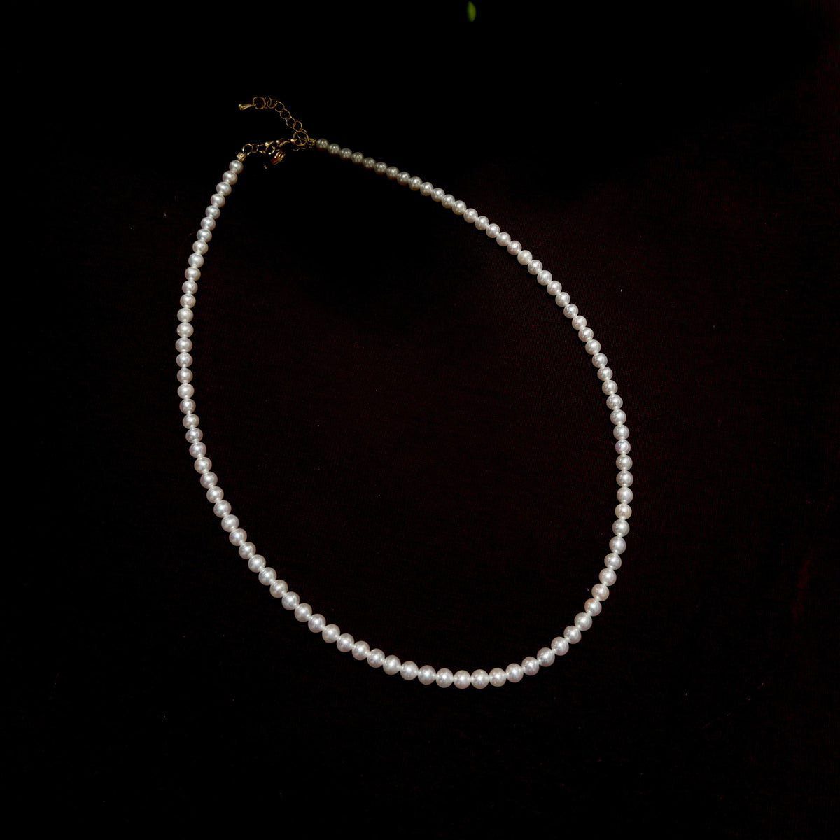 A single-strand pearl necklace with a gold clasp, displayed on a dark black background.
