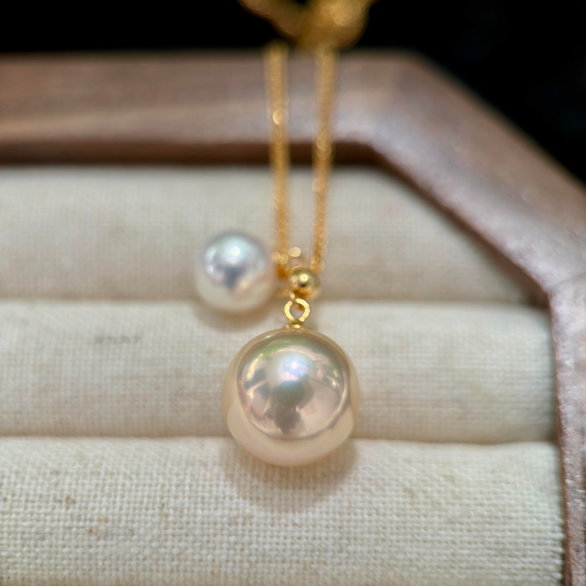 A gold necklace with a large, lustrous white pearl pendant displayed on a beige jewelry cushion.