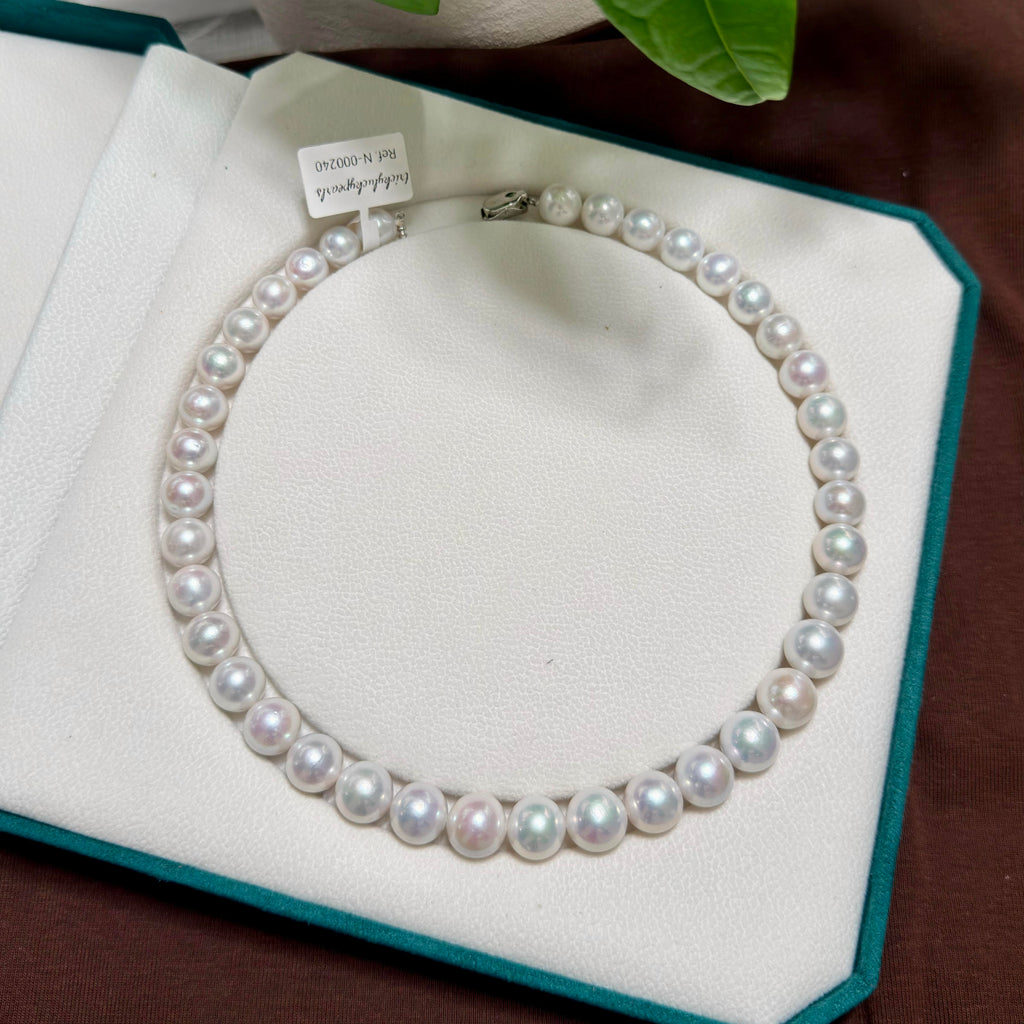 A strand pearl necklace arranged in a circle on a white jewelry display cushion inside an open teal box. The pearls are white with soft pearly luster and are secured by a silver clasp.