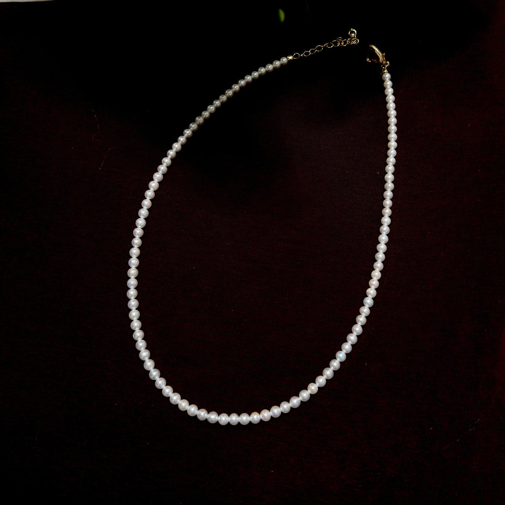 A single-strand pearl necklace with a gold clasp and extender chain, displayed on a dark, nearly black background.