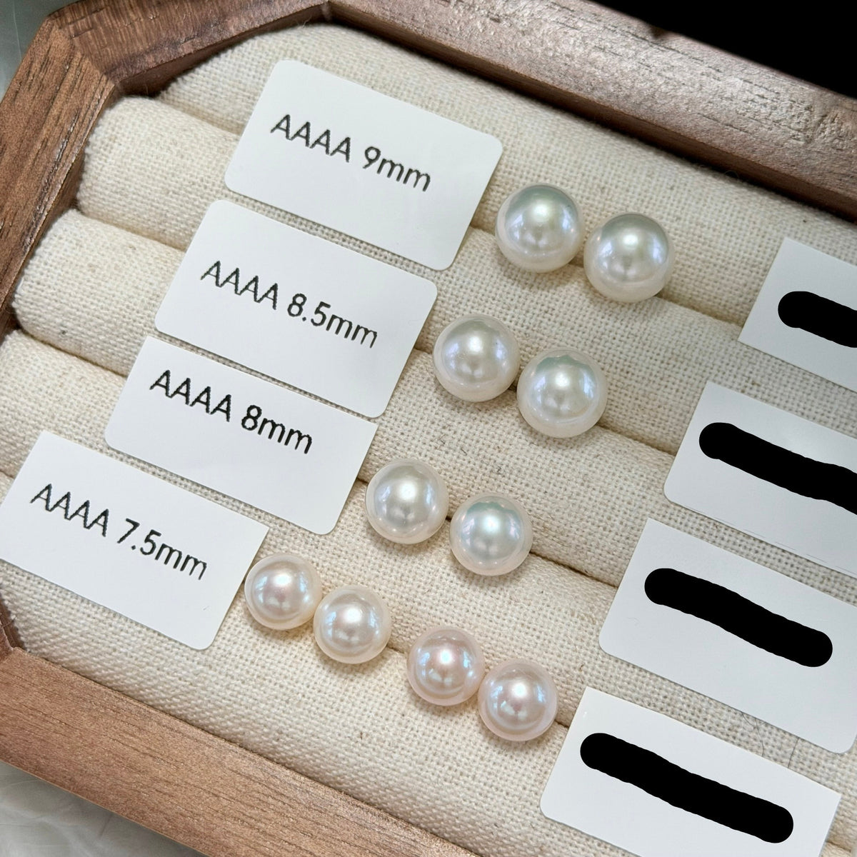 Four pairs of white freshwater pearl stud earrings displayed in a wooden tray with size labels reading AAAA 9mm, AAAA 8.5mm, AAAA 8mm, and AAAA 7.