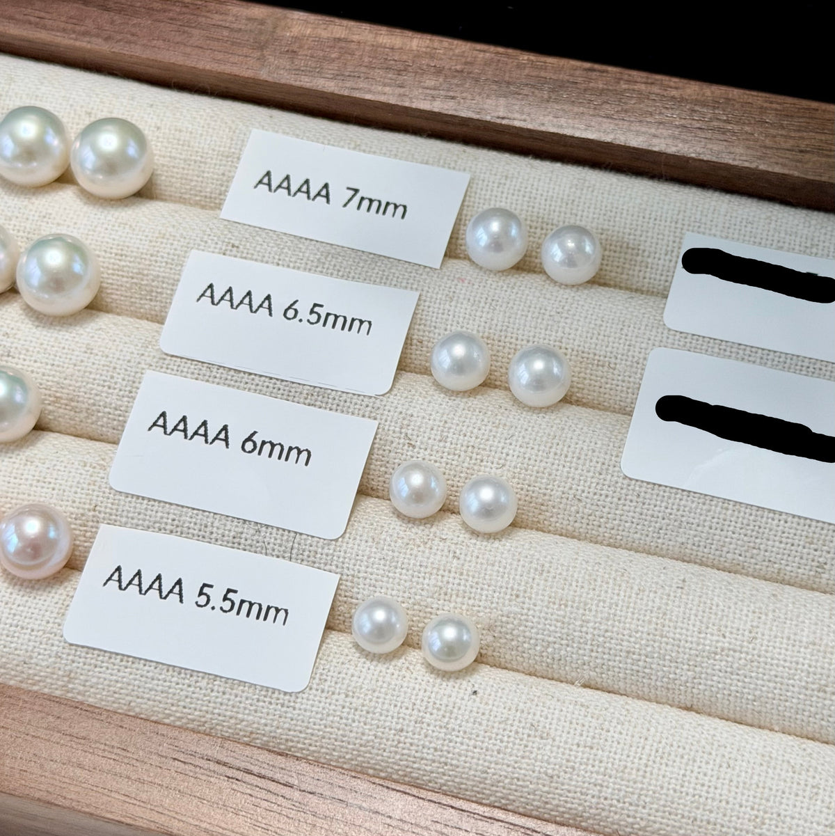 White freshwater pearl stud earrings displayed in a wooden jewelry box with size labels indicating AAAA 7mm, AAAA 6.5mm, AAAA 6mm, and AAAA 5.