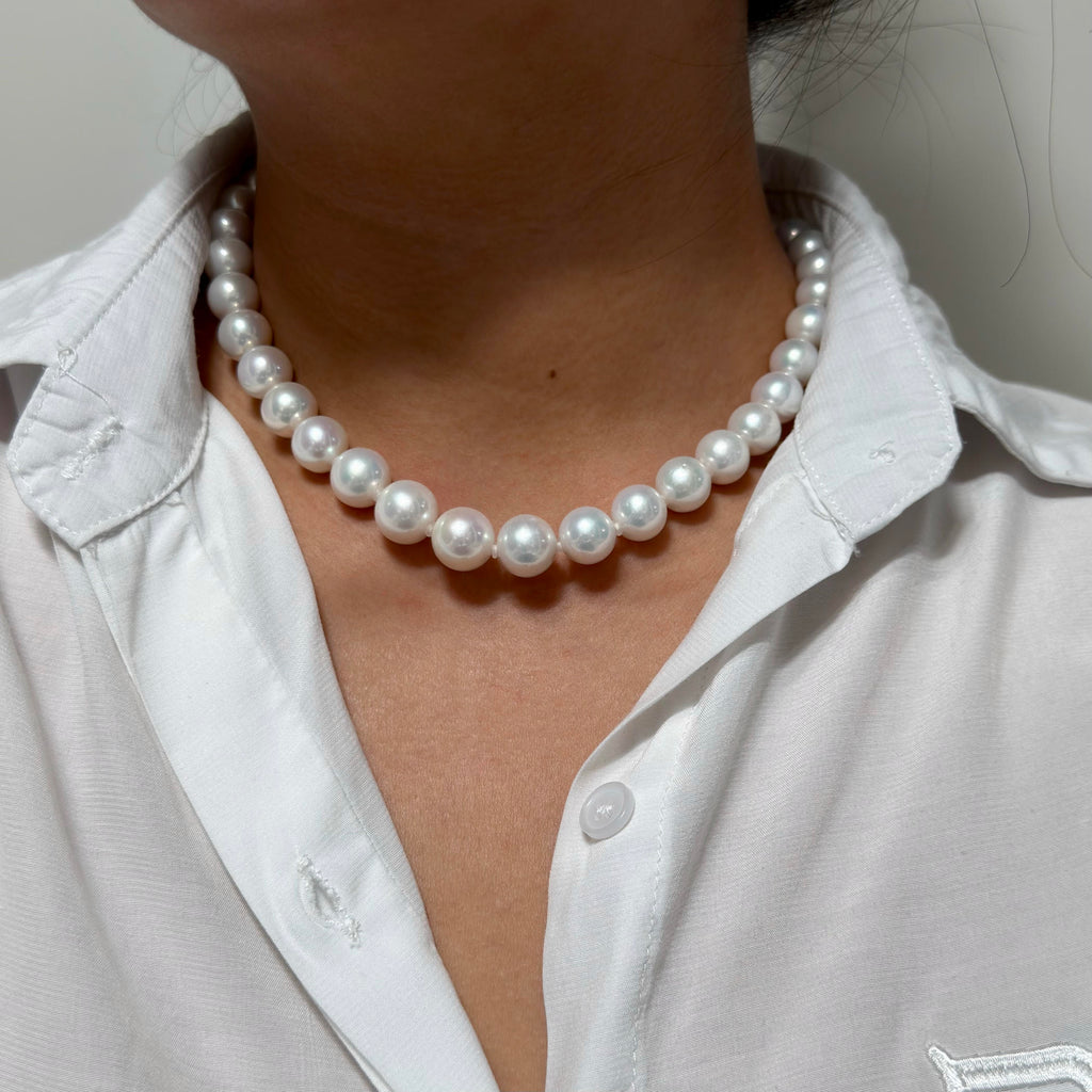 A close-up of a person wearing a classic white freshwater pearl necklace with a white collared shirt.