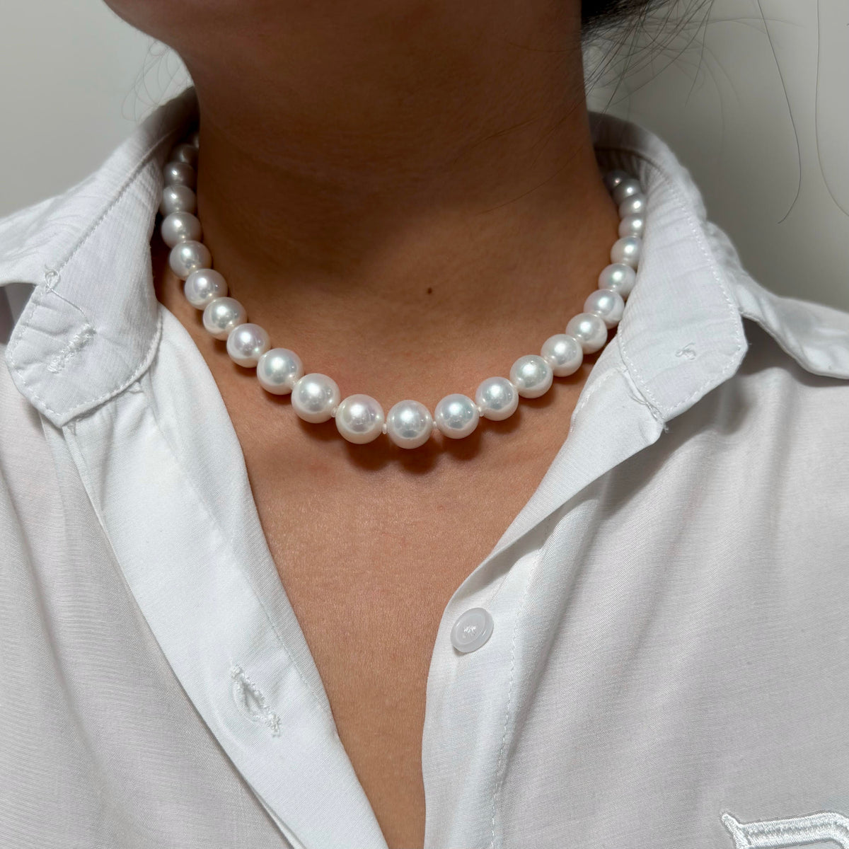 A close-up of a person wearing a classic white freshwater pearl necklace with a white collared shirt.