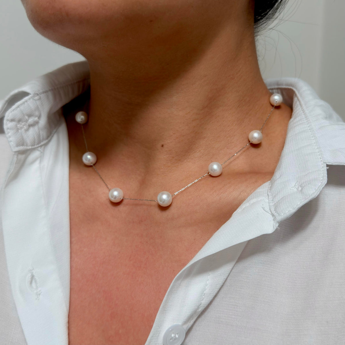 Model wearing a minimalist 8.5 mm white freshwater pearl station necklace with pink halo.
