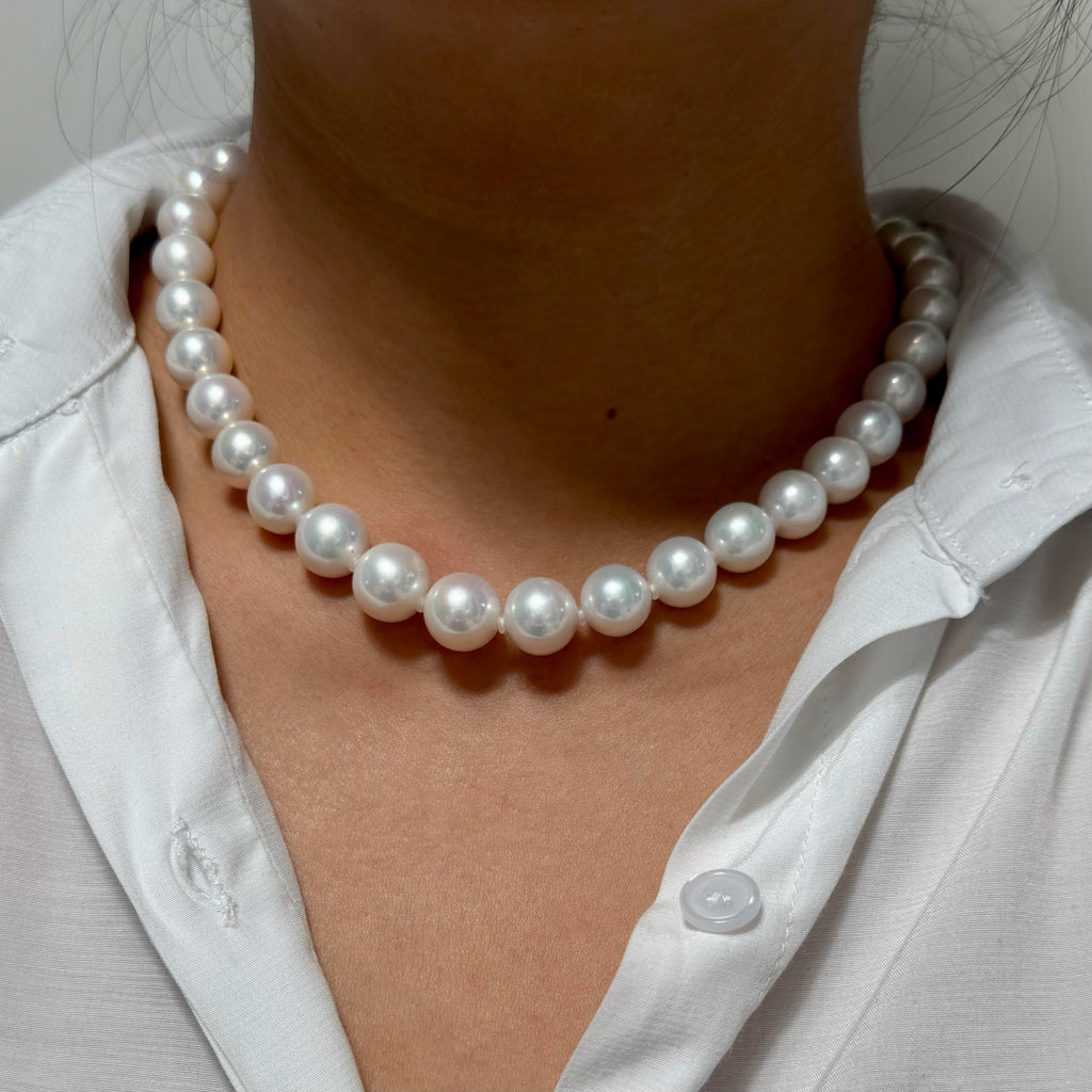 A close-up of a person wearing a classic white freshwater pearl necklace with a white collared shirt.
