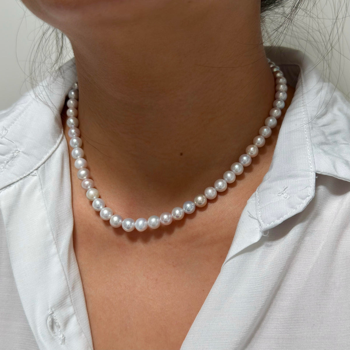 A close-up of a person wearing a classic white pearl necklace with a white collared shirt.