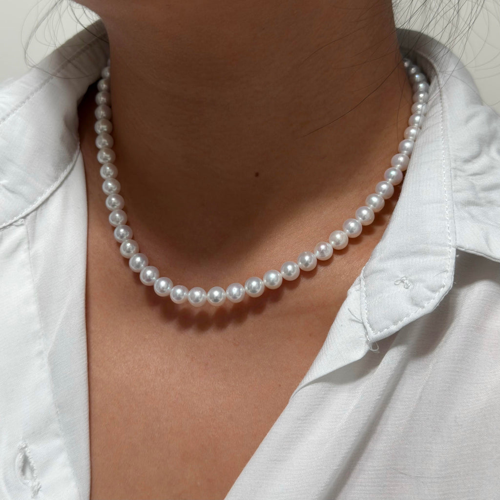 A close-up of a person wearing a classic white pearl necklace with a white collared shirt.