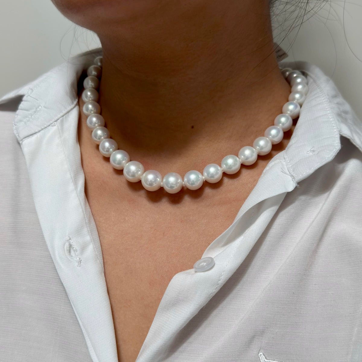 A close-up of a person wearing a classic white pearl necklace with lustrous white beads, styled with a white collared shirt.