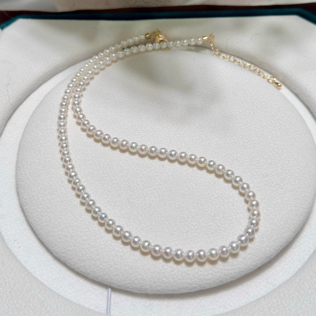 A double-strand pearl necklace with gold clasp, displayed on a white circular jewelry stand.