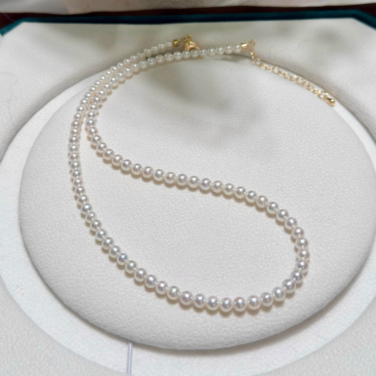A double-strand pearl necklace with gold clasp, displayed on a white circular jewelry stand.