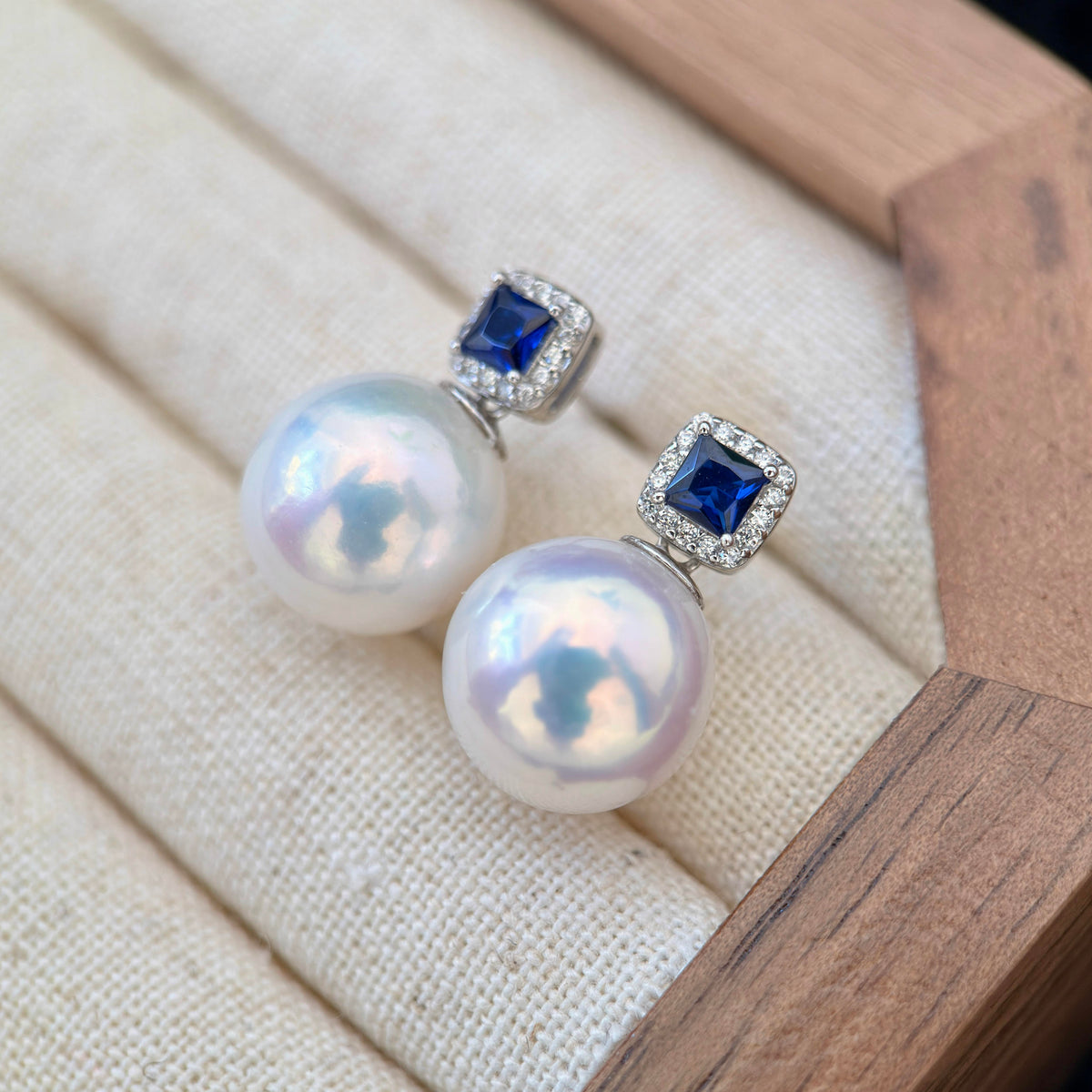 White pearl earrings displaying a striking cool blue iridescent halo.
