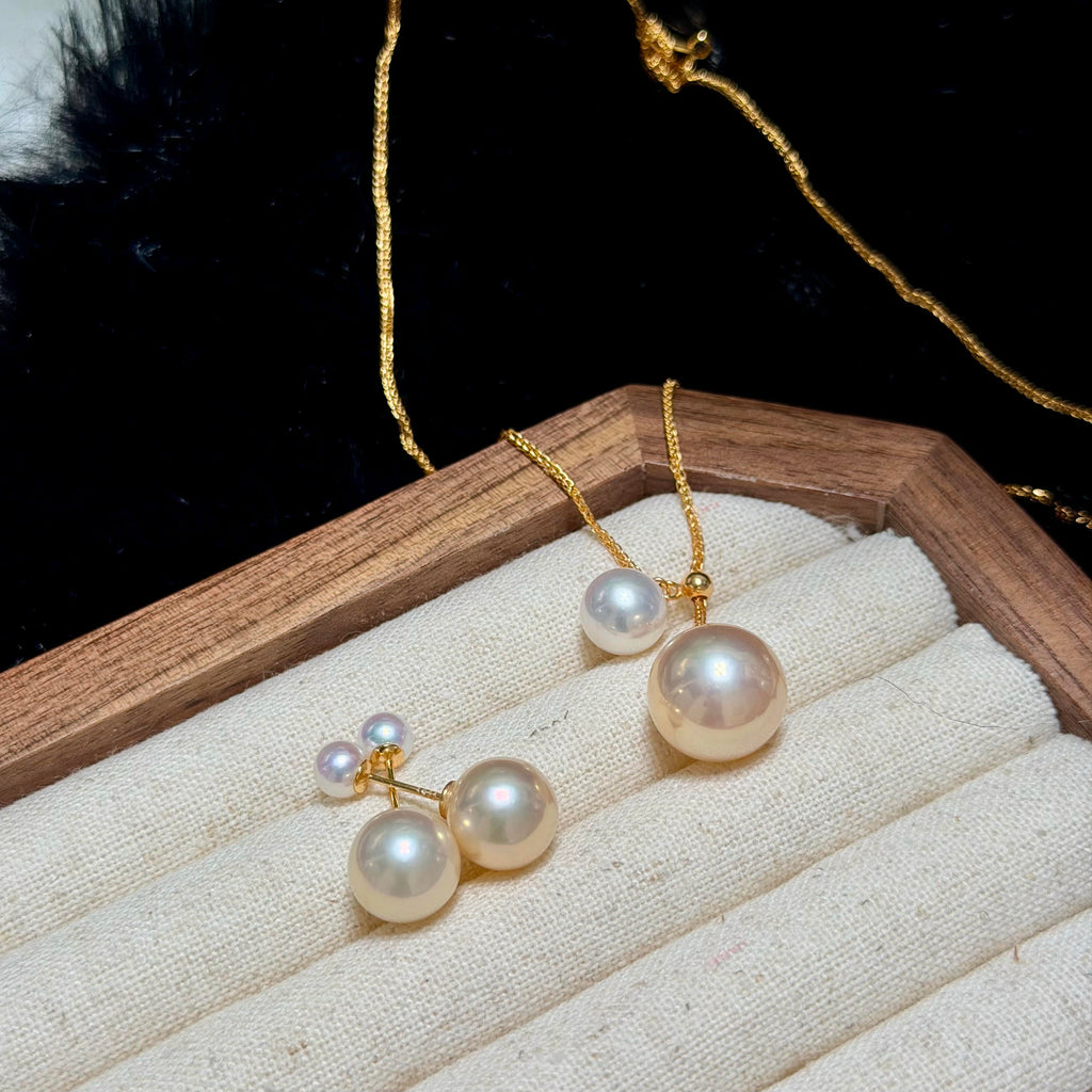 Gold necklace and matching drop earrings with large white pearls, displayed on a cream fabric jewelry tray with a wooden frame against a black background.