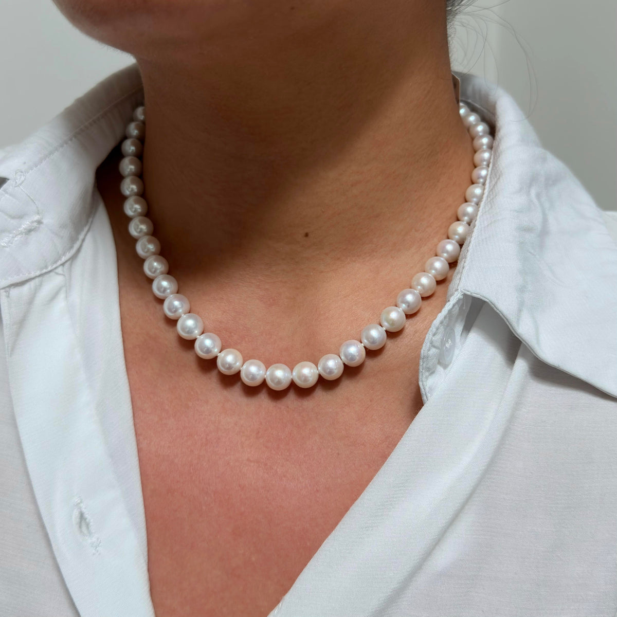 A close-up of a person wearing a classic white pearl necklace with white pearls, styled with a white collared shirt.
