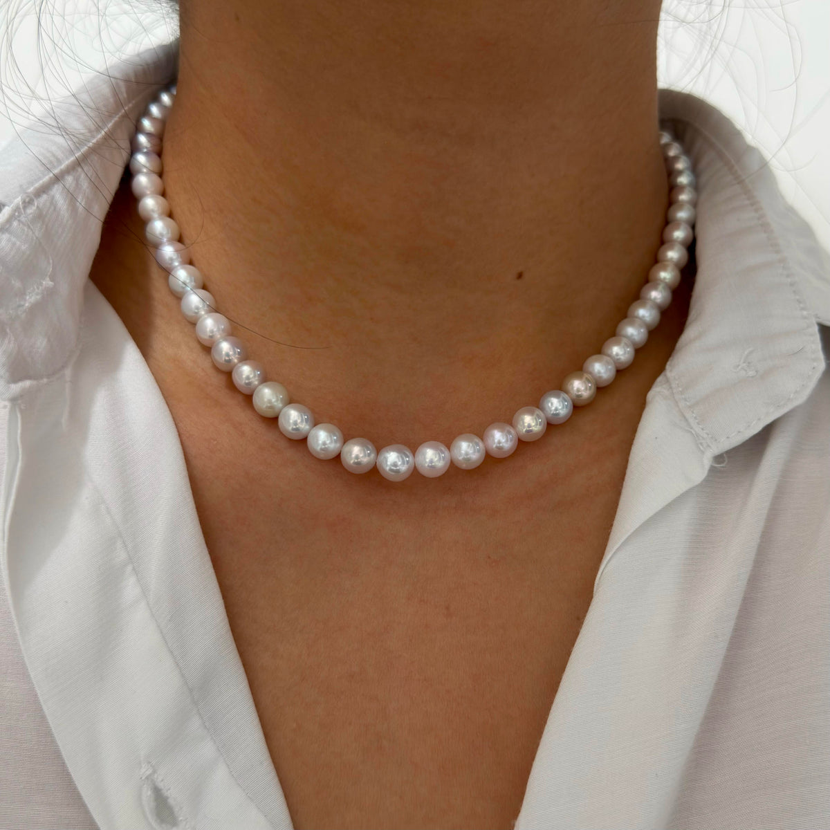 A close-up of a person wearing a classic double-strand pearl necklace with a white collared shirt.