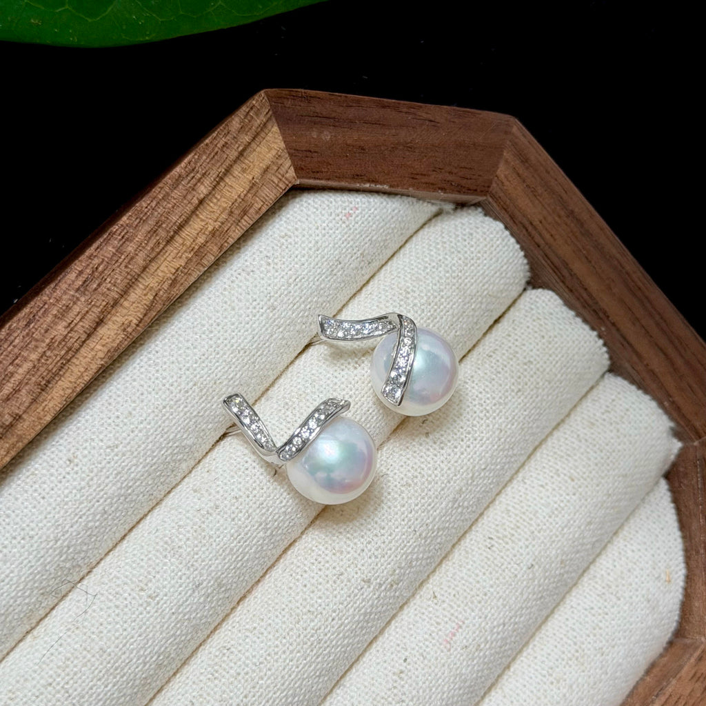 A pair of silver hoop earrings with white freshwater pearls and small clear stones, displayed on a cream fabric-lined wooden jewelry box.