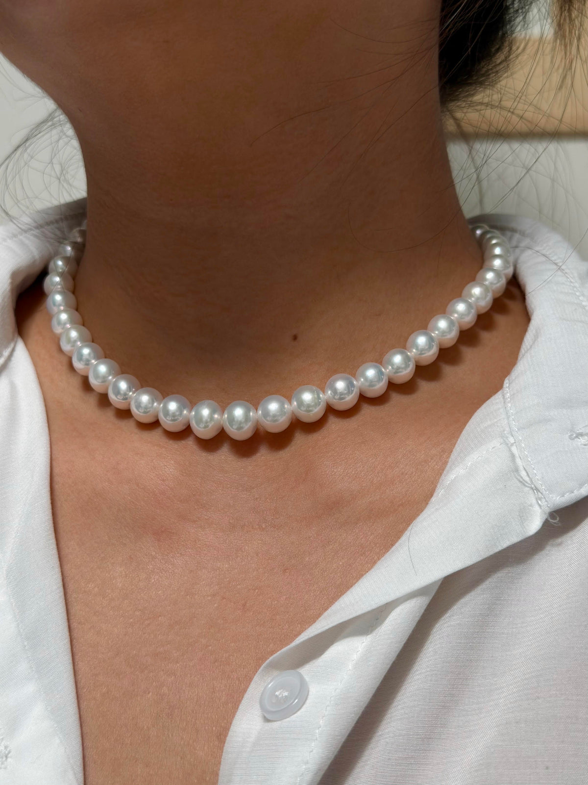 A close-up of a person wearing a classic single-strand white pearl choker necklace with a white collared shirt.