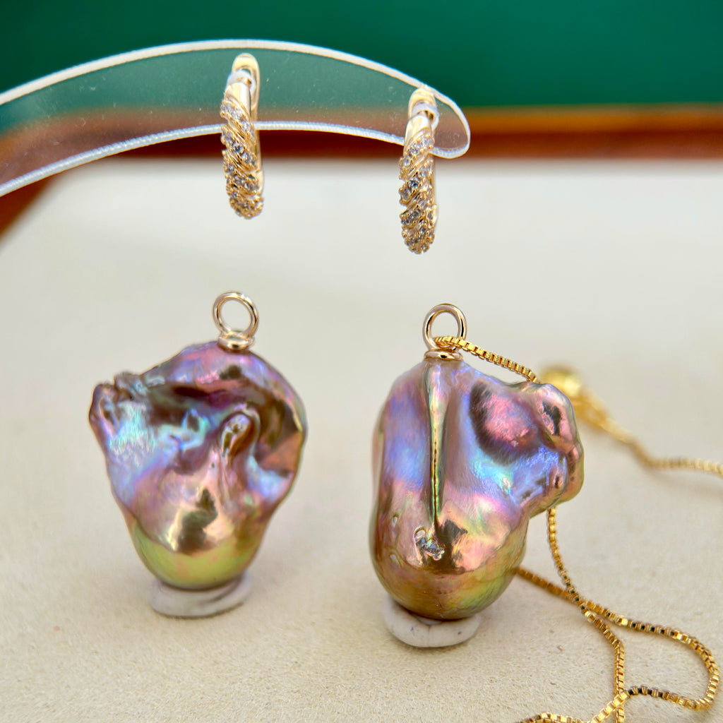 Gold jewelry set featuring a baroque pearl pendant necklace and matching hoop earrings, displayed on clear stands against a neutral background.