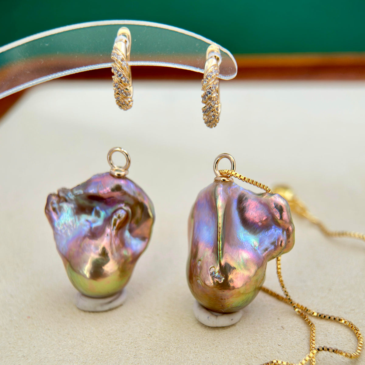 Gold jewelry set featuring a baroque pearl pendant necklace and matching hoop earrings, displayed on clear stands against a neutral background.