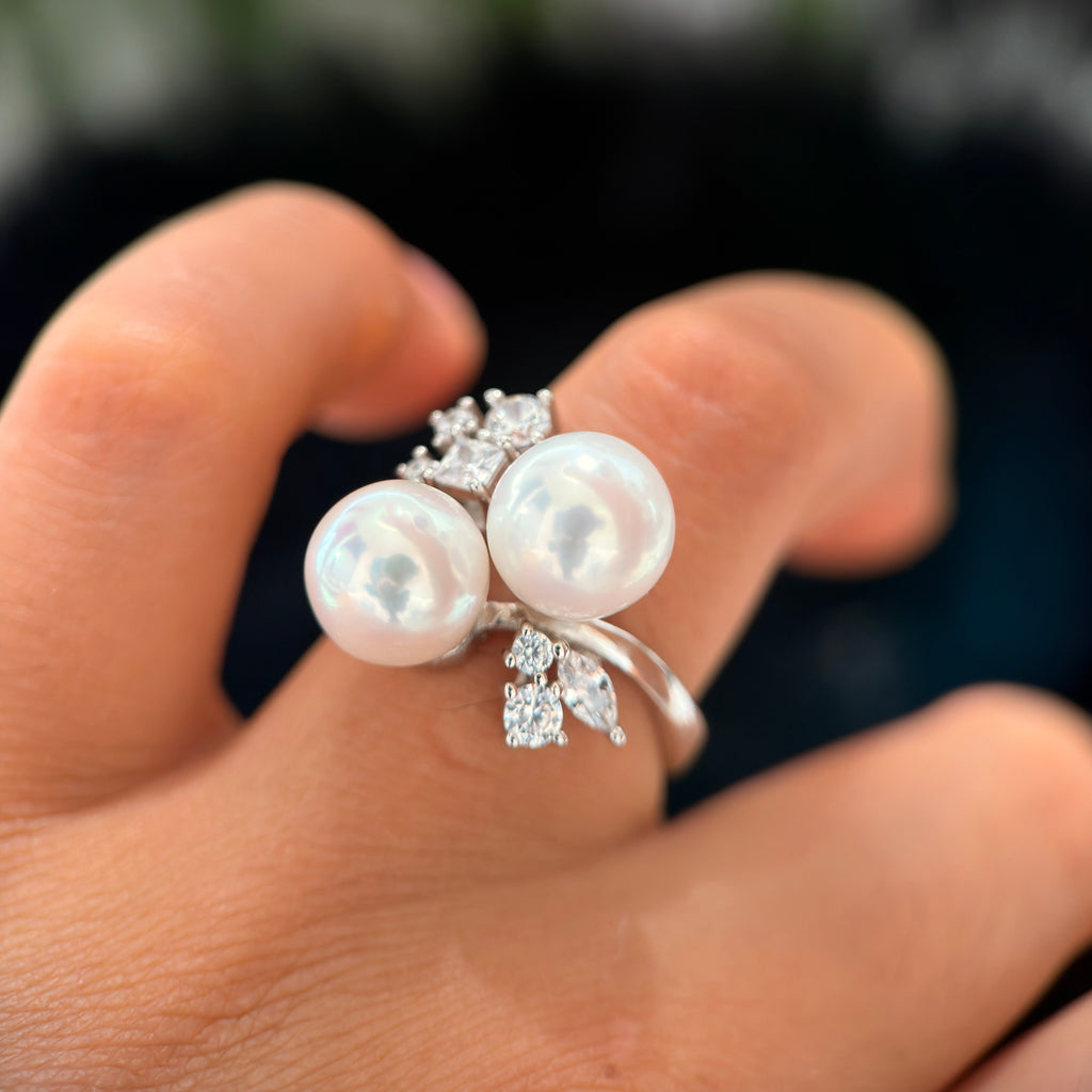 A close-up of a hand wearing a silver ring with two large white pearls and small clear crystal leaf accents.