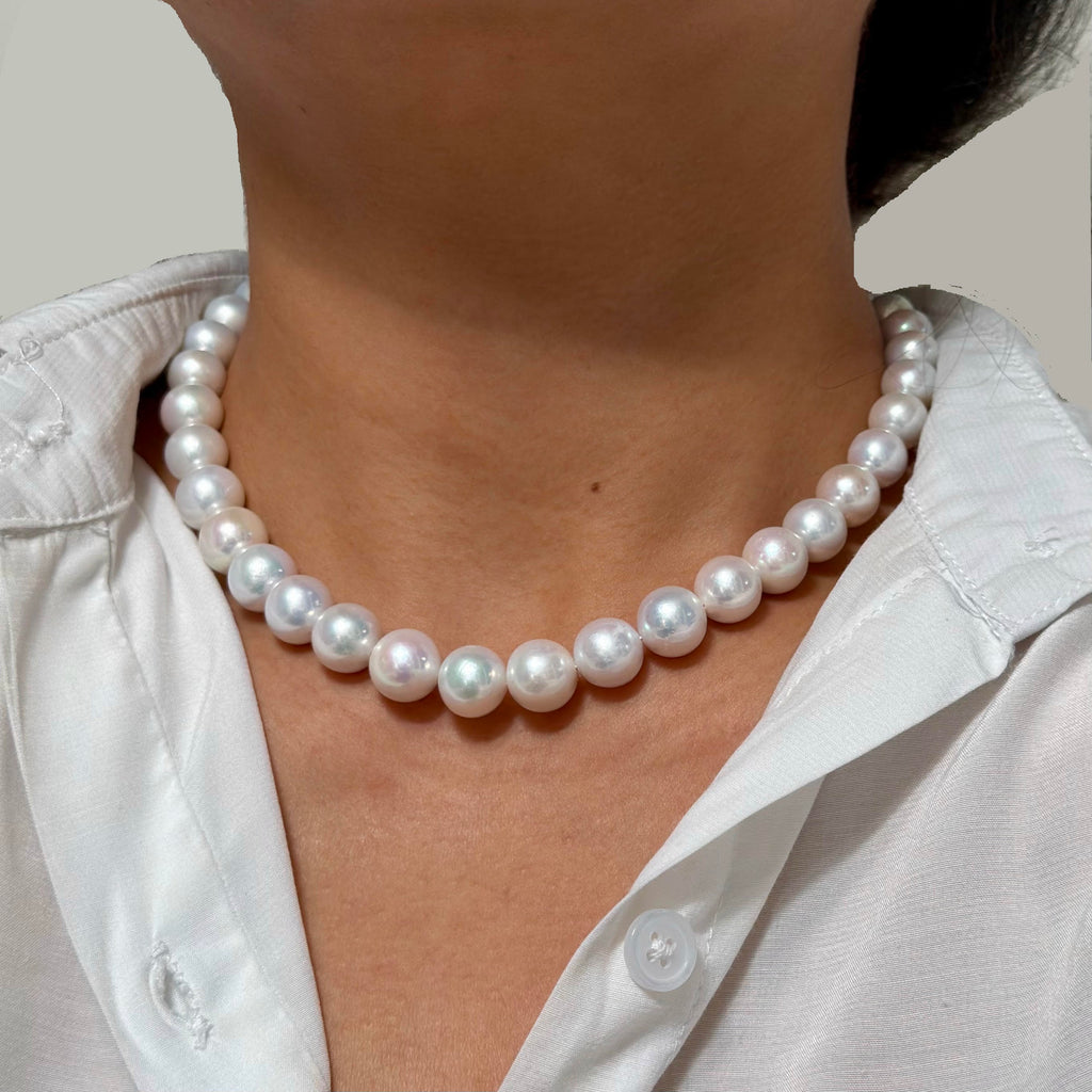 A close-up of a person wearing a classic white freshwater pearl necklace with a white collared shirt.