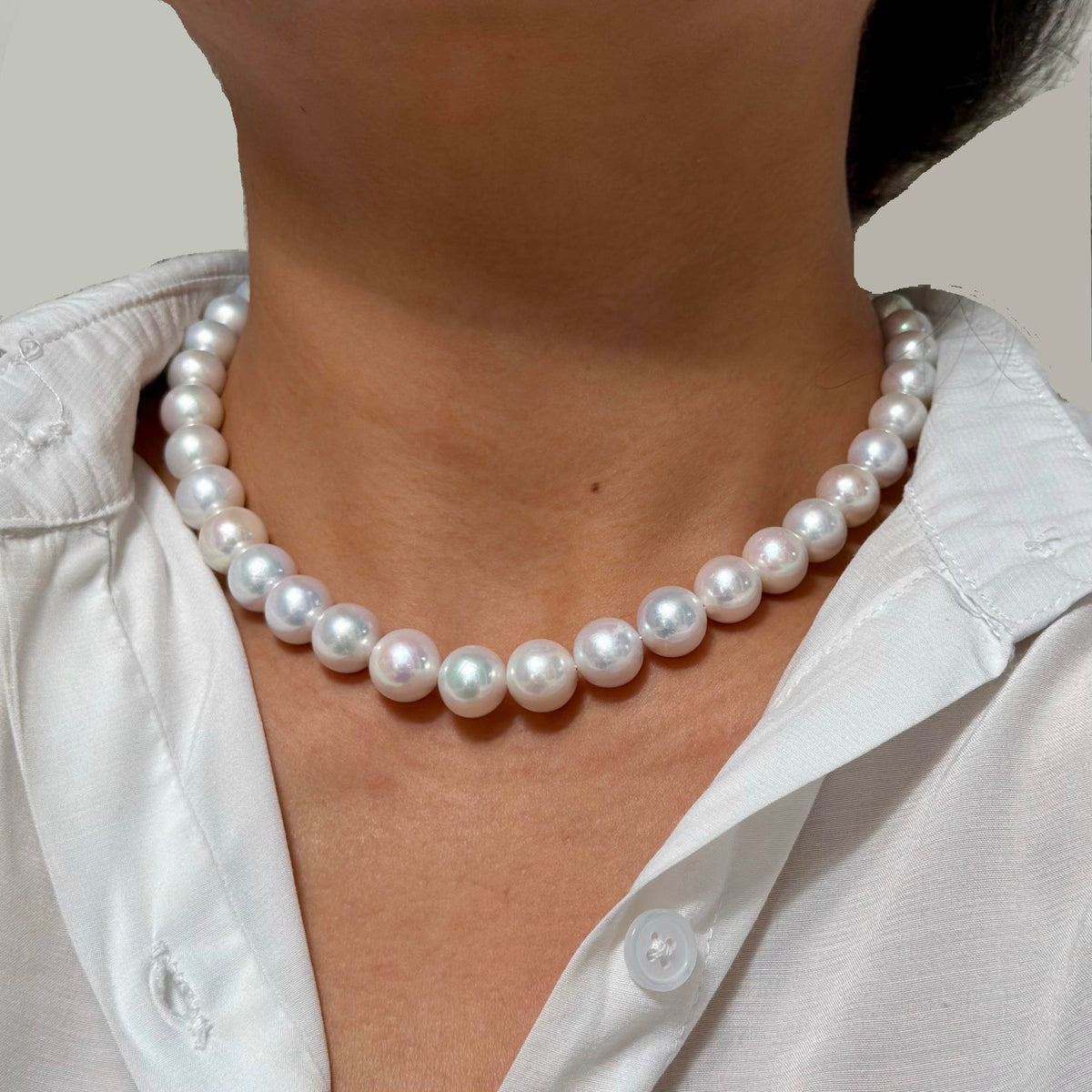 A close-up of a person wearing a classic white freshwater pearl necklace with a white collared shirt.