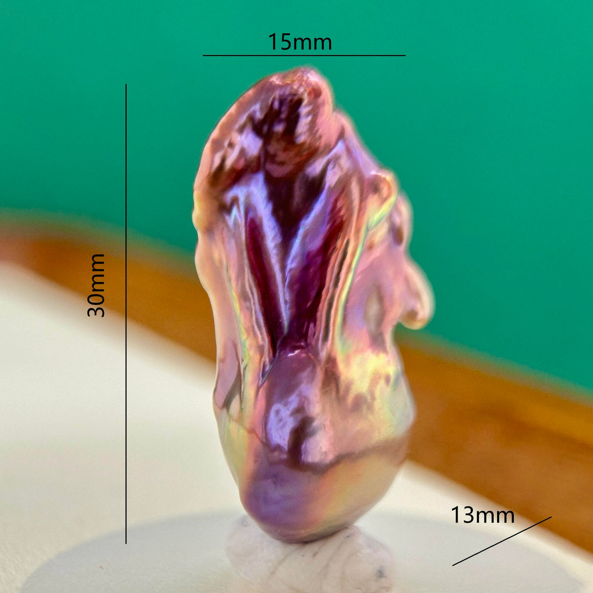 A small iridescent shell-like decorative object shown upright on a white surface, with measurement lines and labels indicating 30mm height, 15mm top width, and 13mm side depth against a green and beige background.