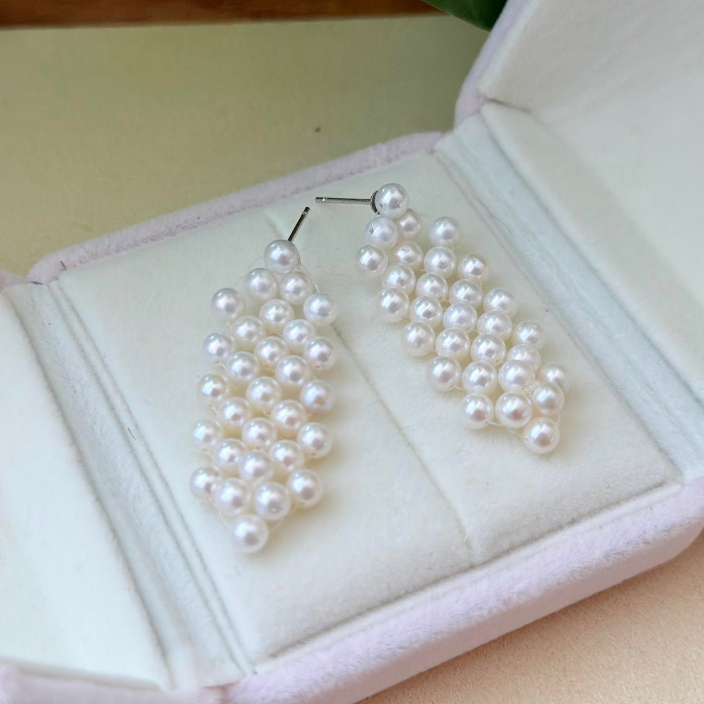 A pair of white pearl drop earrings displayed inside an open light pink jewelry box.