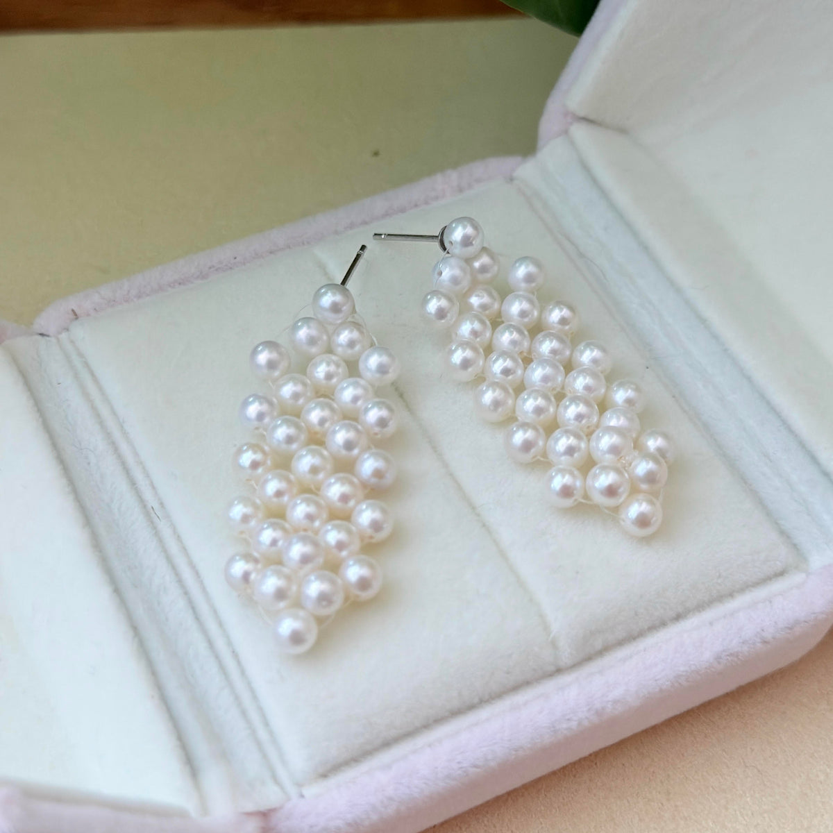 A pair of white pearl drop earrings displayed inside an open light pink jewelry box.