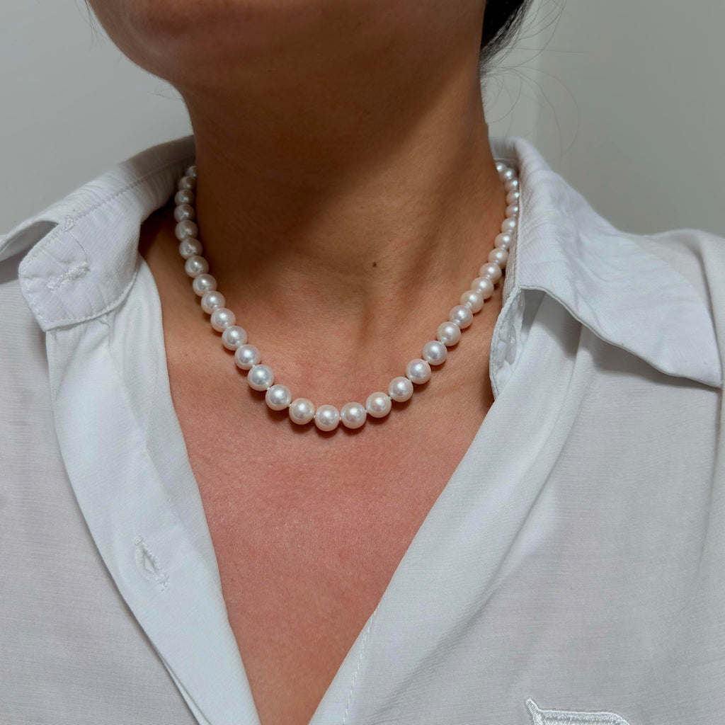 A close-up of a woman wearing a classic white pearl necklace with matching white collared shirt.