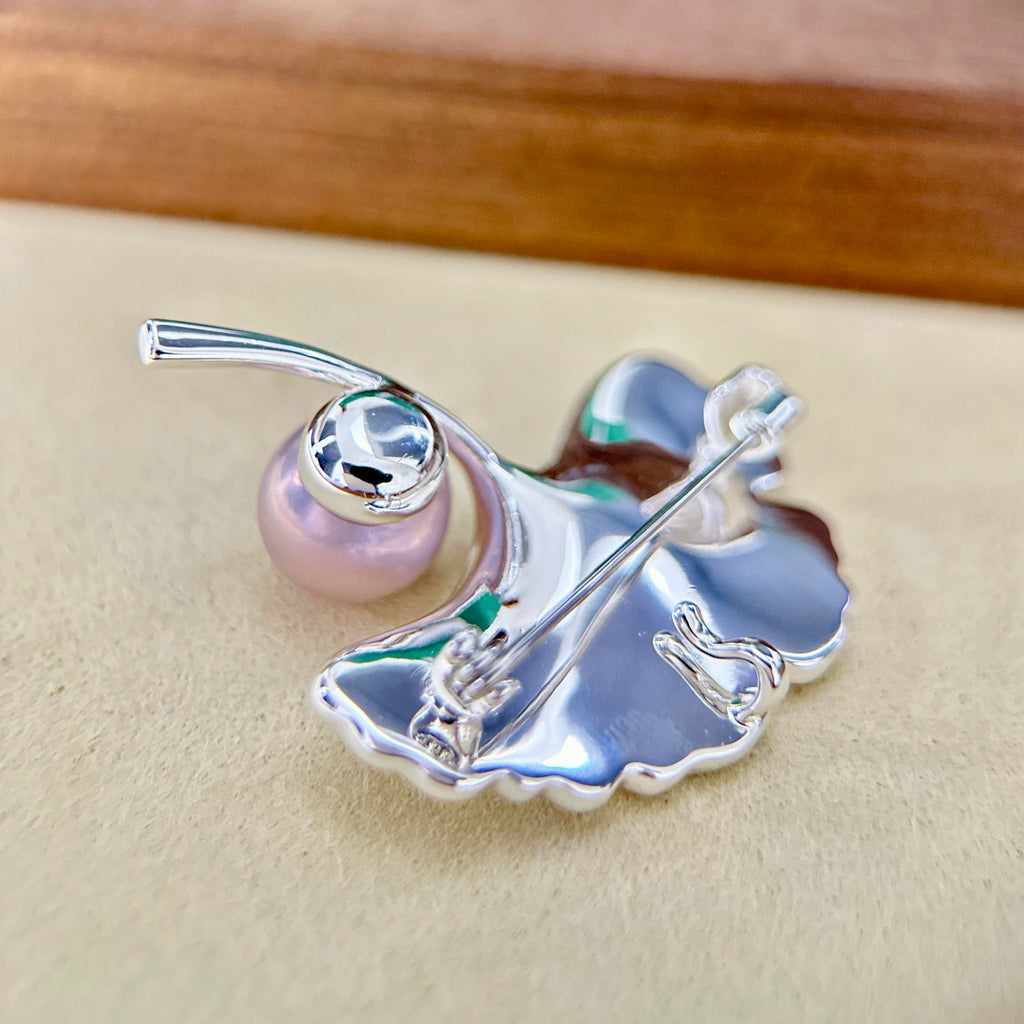 A silver butterfly-shaped brooch with a pink pearl and a clear rhinestone, displayed on a beige surface.