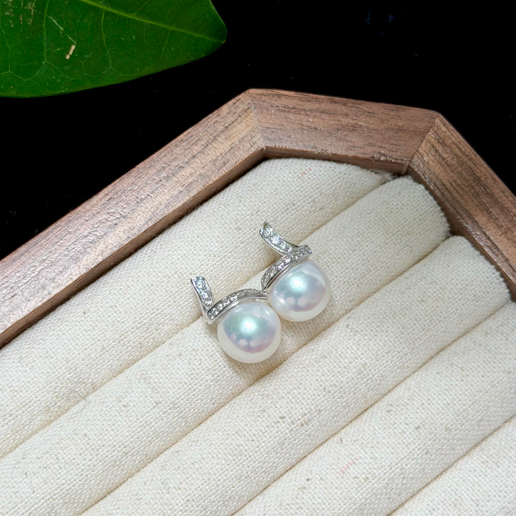 A pair of silver-toned earrings with round iridescent white pearls and small clear stones, displayed on a cream fabric-lined jewelry box inside a wooden tray.