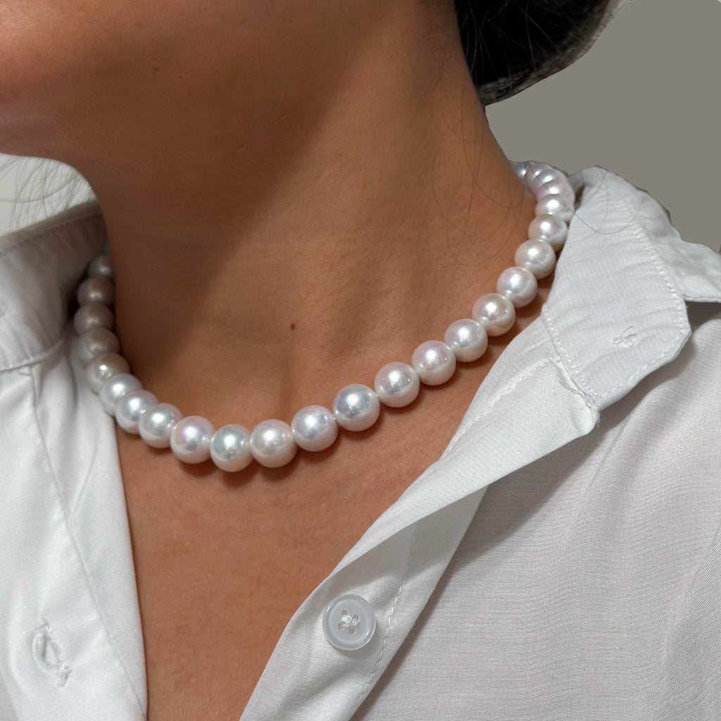 A close-up of a person wearing a classic white freshwater pearl necklace with a white collared shirt.