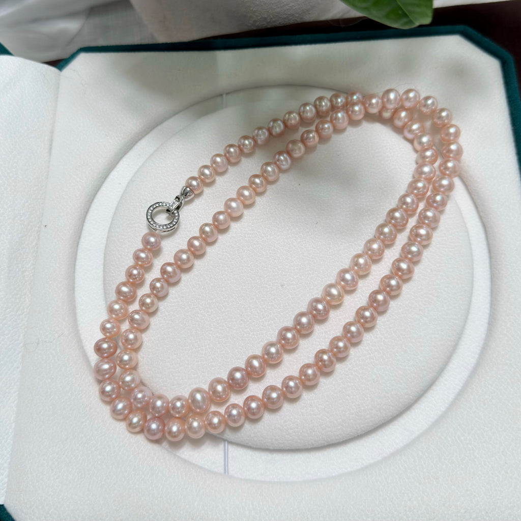 A double-strand pink freshwater pearl necklace with a silver clasp, displayed inside an open white jewelry box.