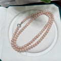 A double-strand pink freshwater pearl necklace with a silver clasp, displayed inside an open white jewelry box.