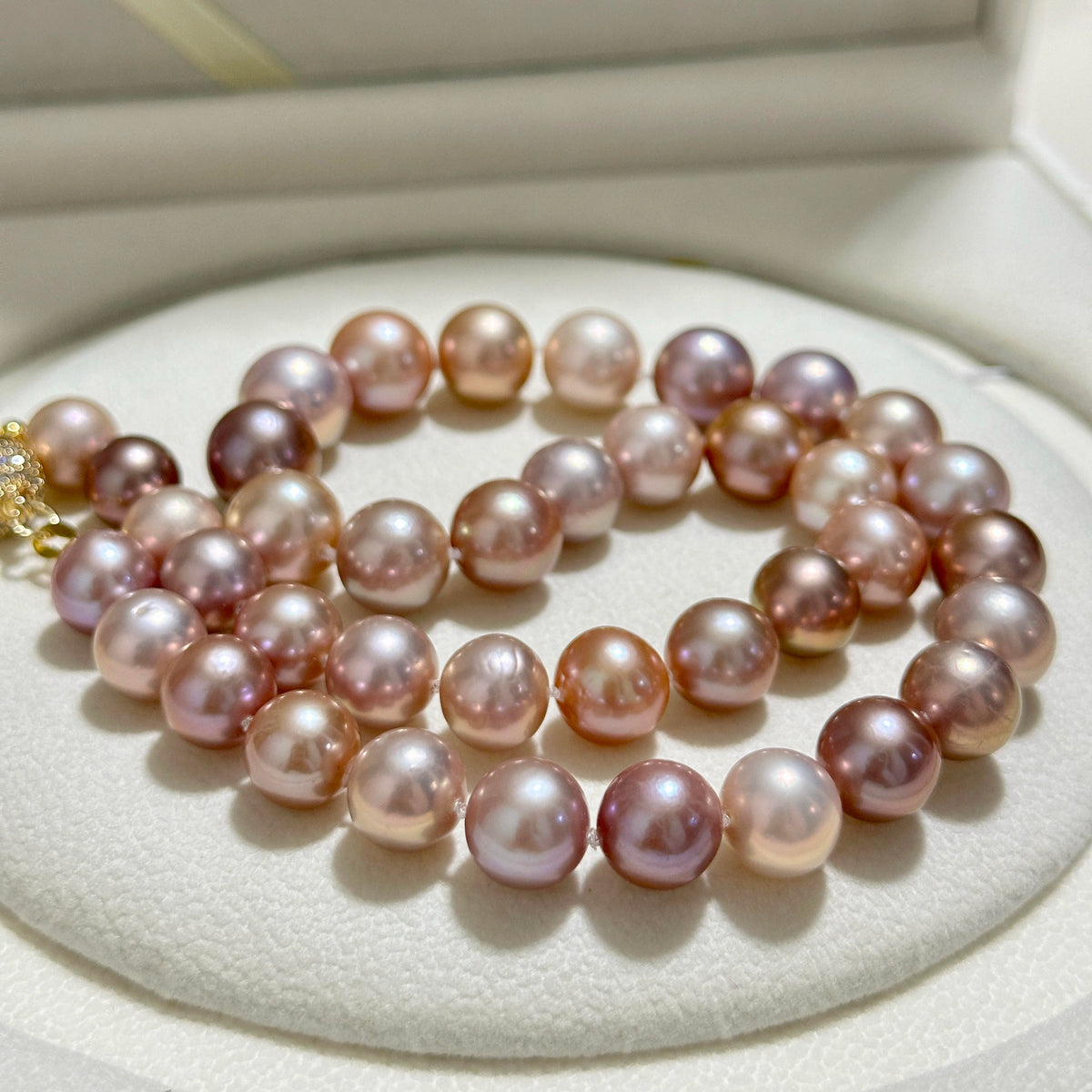 A strand of pink freshwater pearls with a gold clasp, displayed on a white textured jewelry stand.