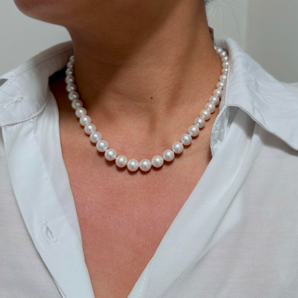 A close-up of a person wearing a classic white pearl necklace with a white collared shirt.