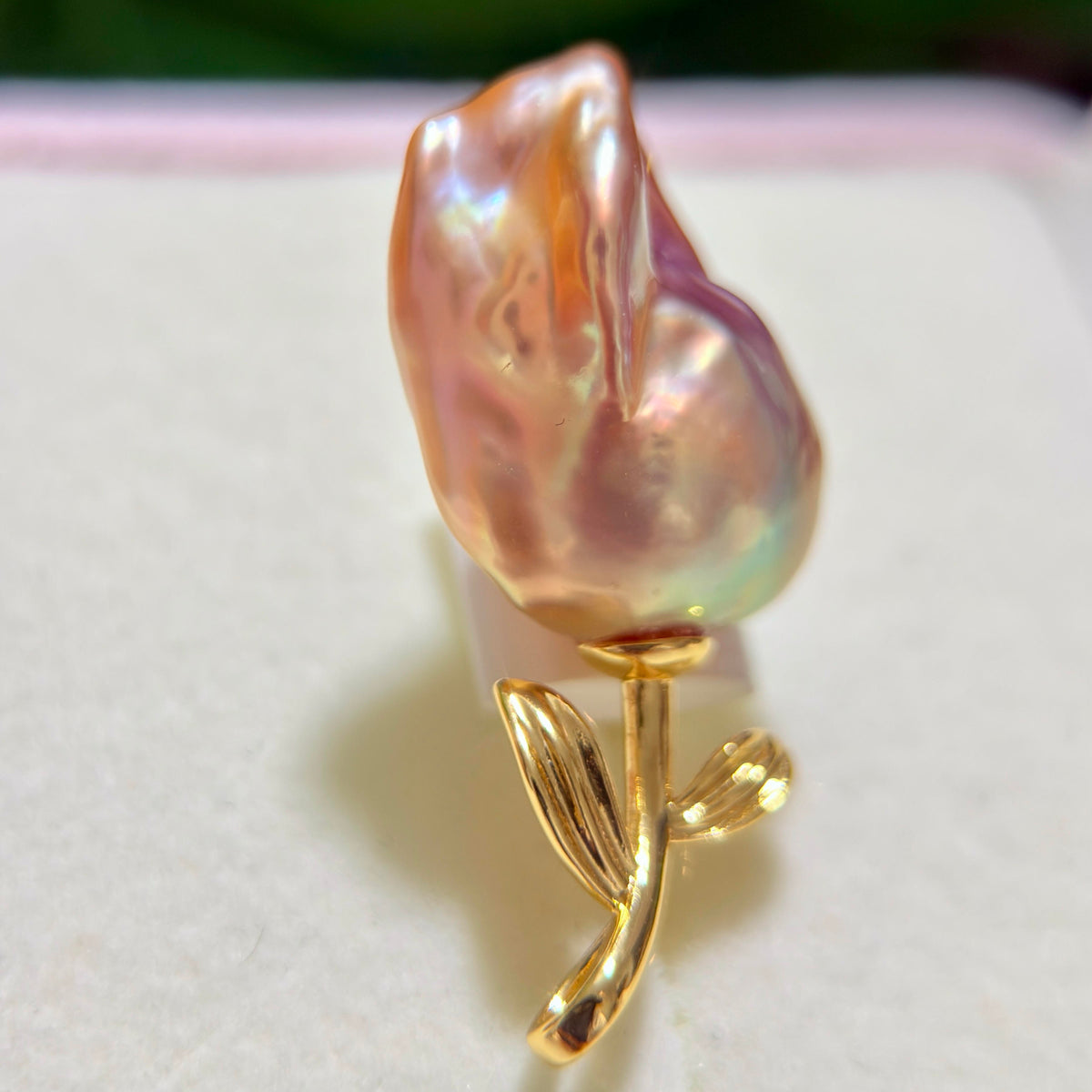 A baroque pearl rose ring featuring a large, irregularly shaped pearl with iridescent pink, purple, and green hues on a polished gold setting with a stem and leaves.