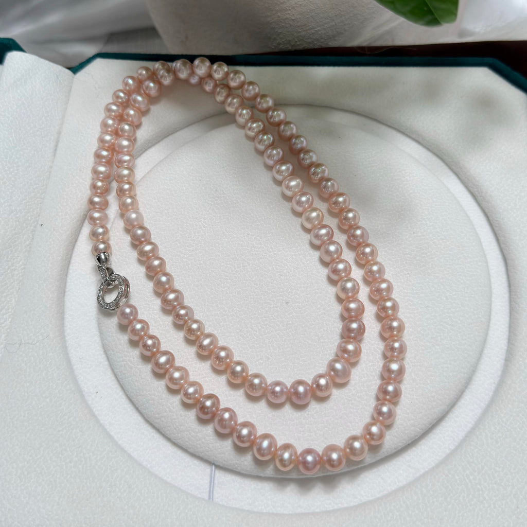A double-strand pink freshwater pearl necklace with a silver clasp, displayed on a white circular jewelry stand inside an open presentation box.