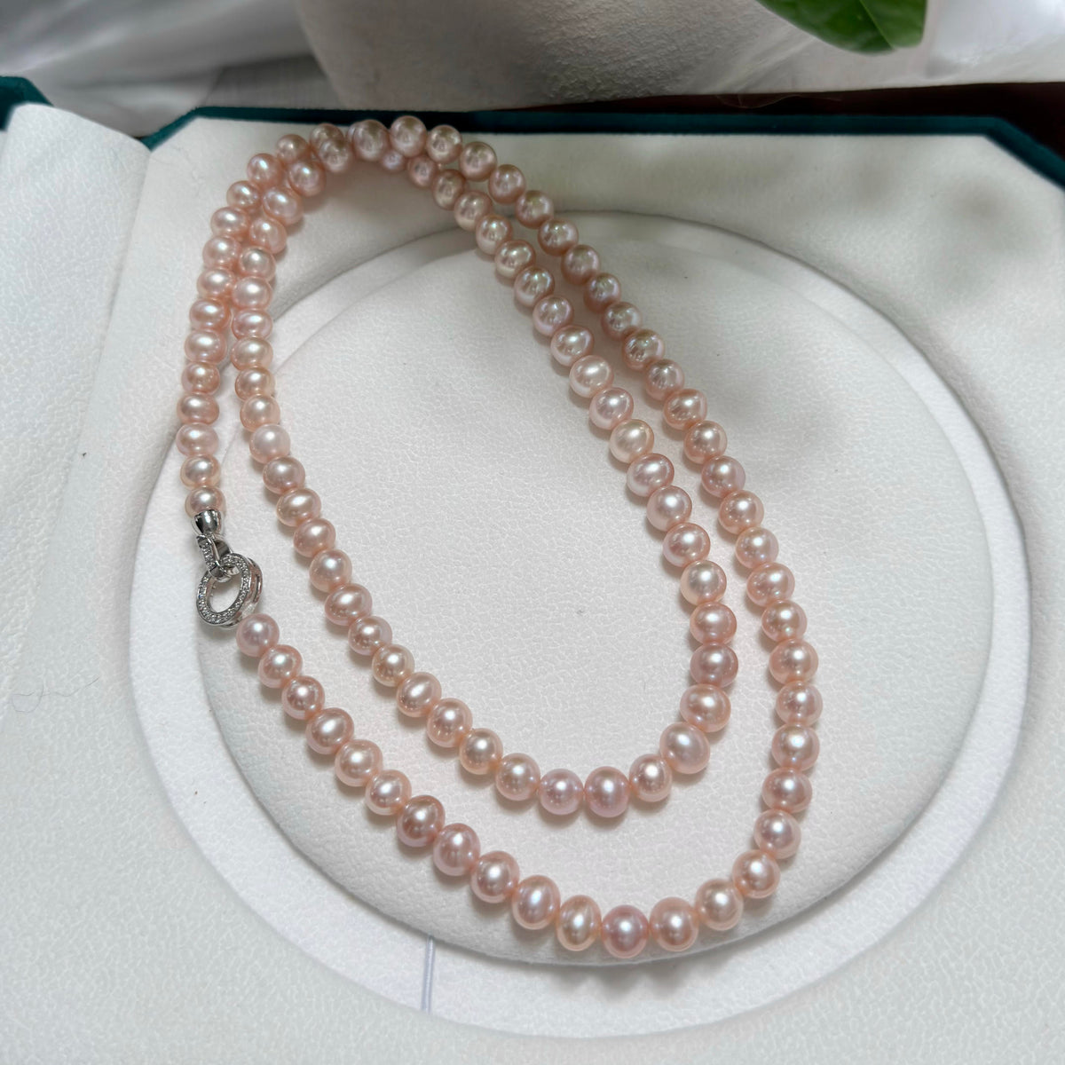 A double-strand pink freshwater pearl necklace with a silver clasp, displayed on a white circular jewelry stand inside an open presentation box.