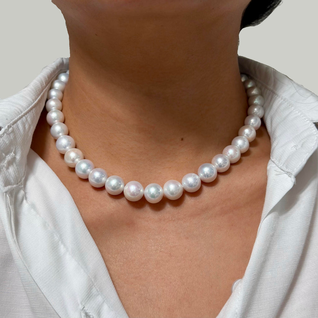 A close-up of a person wearing a classic white bright freshwater pearl necklace with a white collared shirt, showing the pearls resting on the neck.