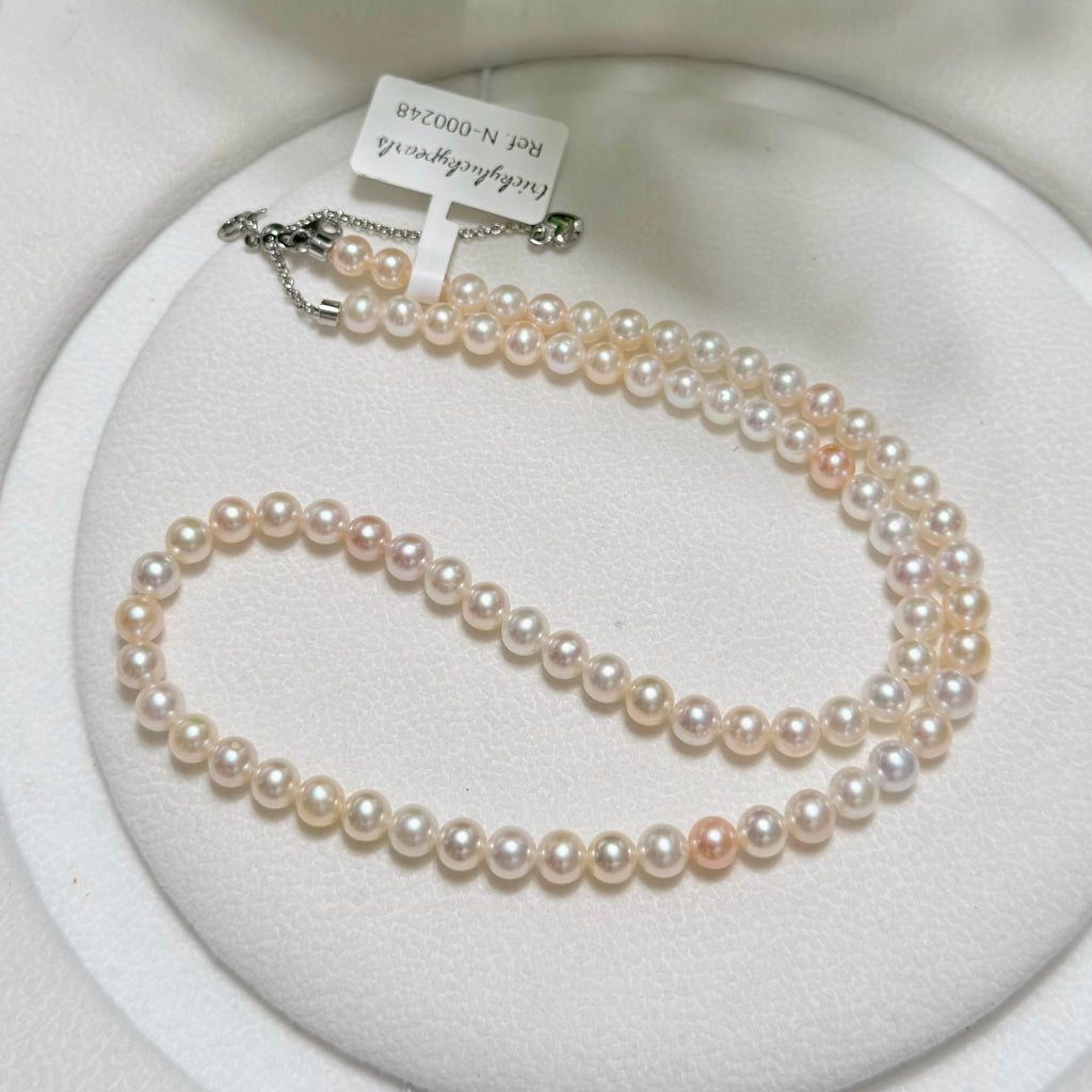 A double-strand pearl necklace with white and pale pink pearls, displayed on a white circular jewelry stand. A small paper tag is attached near the clasp, which is silver-toned metal.